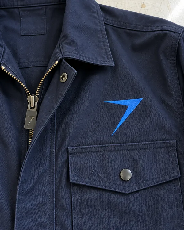 The chest of a dark navy coverall: a zipper under a folded-back flap, a snap pocket and a blue embroidered bolt