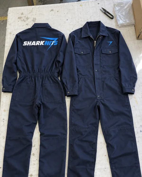 The ALLOY coverall laid flat, back and front: dark navy, with SHARKNITS across the back and a blue bolt on the chest