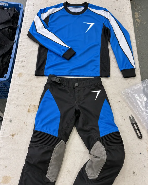 A blue motocross jersey and black and blue pants with gray suede knee panels laid flat