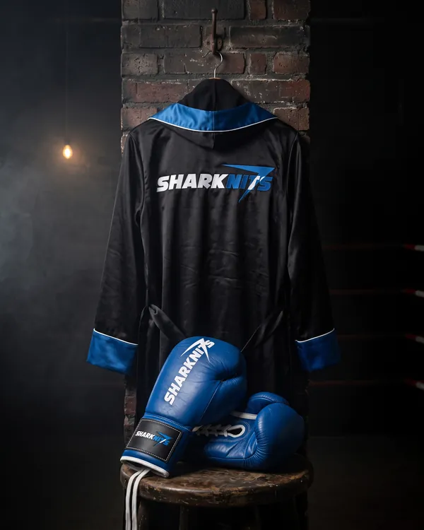 BLUE CORNER hooded robe hanging on a brick wall, with the blue gloves on a wooden stool