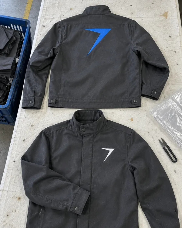 The BRAZE welding jacket laid flat, back and front: charcoal, with a large blue bolt on the back and a white bolt on the chest