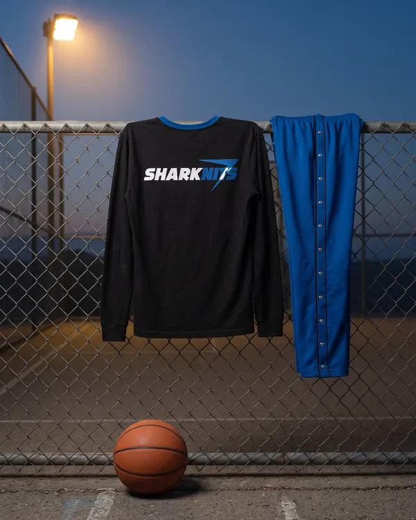 COURTSIDE long sleeve tee and blue snap pants hanging on a court fence