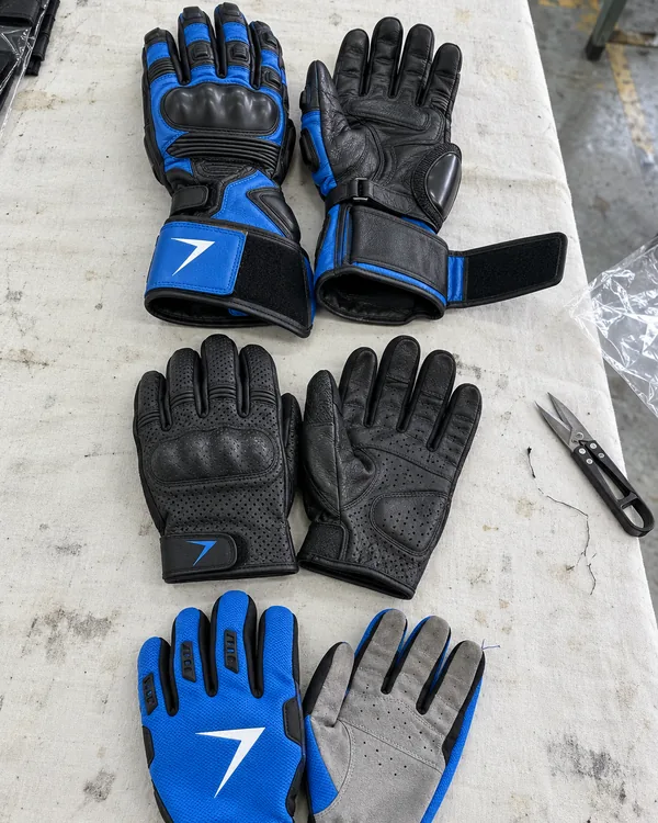 Race gauntlets, short cuff gloves and blue motocross gloves laid flat on a white table sheet