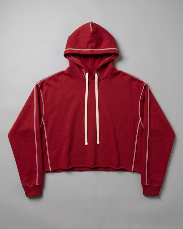 RAW cropped hoodie in red, laid flat, with contrast seams on the outside and a raw cut hem