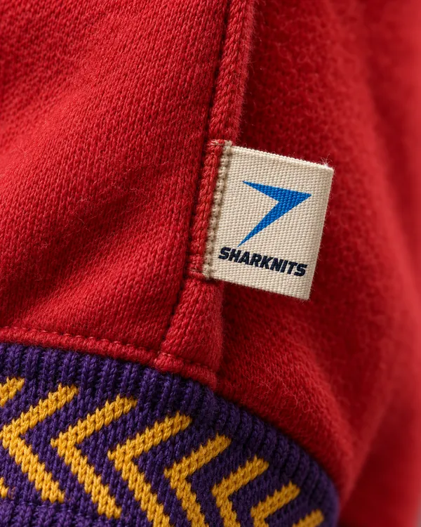 Woven SHARKNITS label sewn into red fleece, above a gold and purple jacquard rib