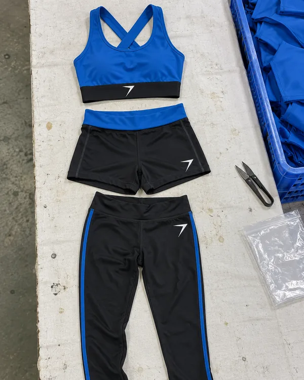 The TEMPO practice set laid flat: a blue crop top with a black hem band, black shorts with a blue waistband and black leggings with a blue stripe