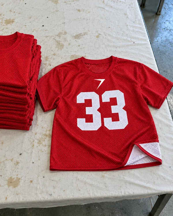 A scarlet mesh practice jersey with a white 33, laid open beside a stack, its hem turned up to show the white side