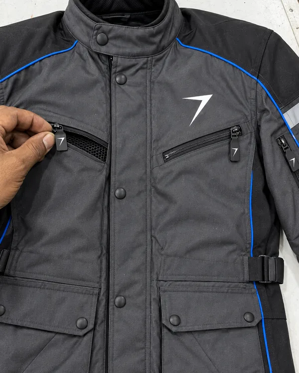 Fingers pull open the zipped chest vent of a charcoal textile riding jacket, showing black mesh