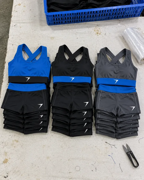 Three stacks of folded practice sets on a table, with blue, black and charcoal crop tops, each over matching shorts