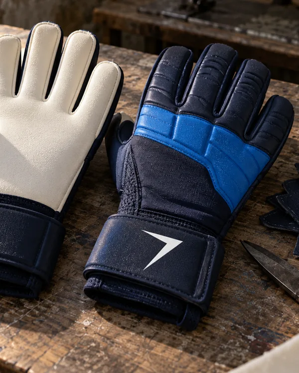 Close up of goalkeeper gloves: a white latex palm, and a navy back with a blue knuckle band and a white bolt on the wrist strap