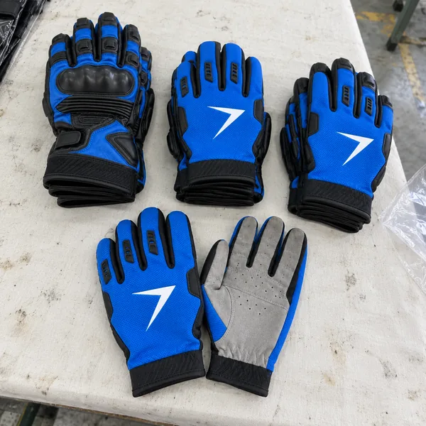 Stacks of blue motocross gloves and short leather gloves, with one more set laid in front, one palm up