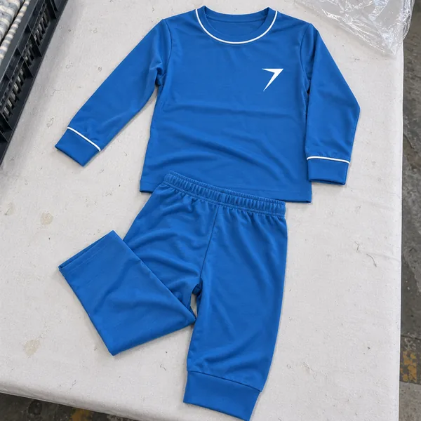 A blue kids pajama set with white piping and a white bolt, laid flat on a cutting table