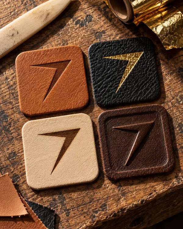 Four leather patches with the bolt: debossed in tan, gold foil on black, laser engraved on cream and embossed in dark brown