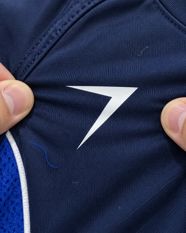 Two thumbs stretch the navy knit around a white bolt logo pressed onto the chest of the PITCH jersey