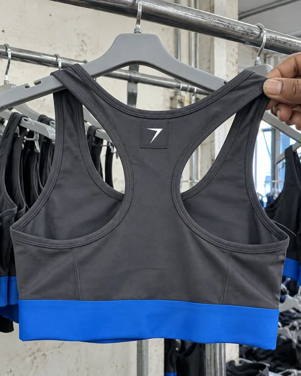 Back of a charcoal racerback sports bra on a hanger, with a woven bolt label and a blue band