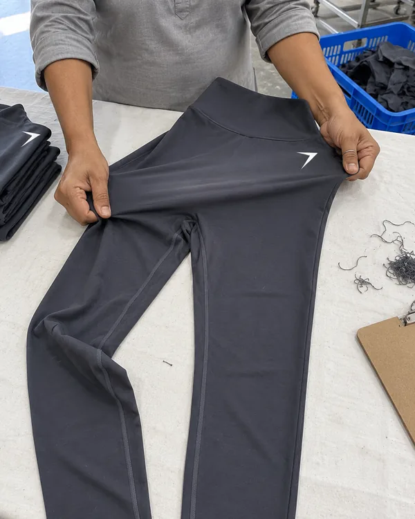 Hands stretch one leg of charcoal leggings across the knuckles at an inspection table