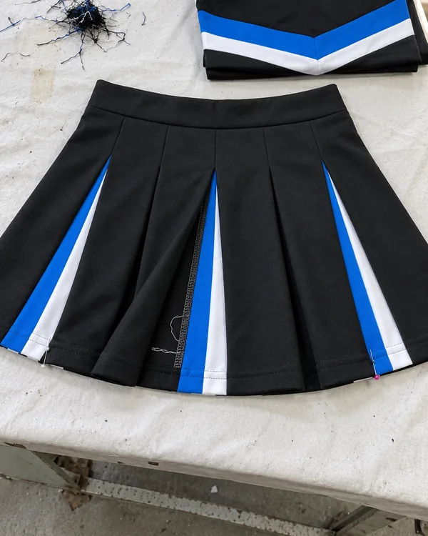 Black pleated skirt pinned open on a table, with blue and white stripes inside the pleats