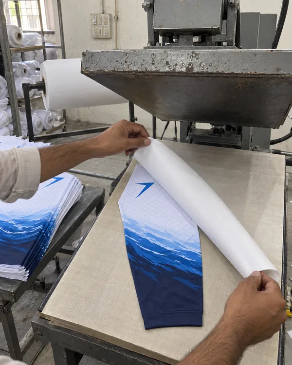 Hands peel printed transfer paper off a TIDE sleeve panel on a heat press