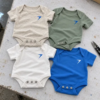 Four baby bodysuits laid flat in oatmeal, sage, white and blue, with snap tabs and a bolt on each chest