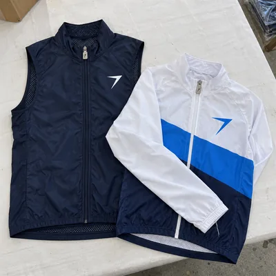 Navy cycling vest and a white and blue cycling jacket laid on a table, each with a bolt