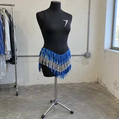 A black stretch leotard with rows of blue and silver fringe at the hips and a bolt in clear stones, on a dress form