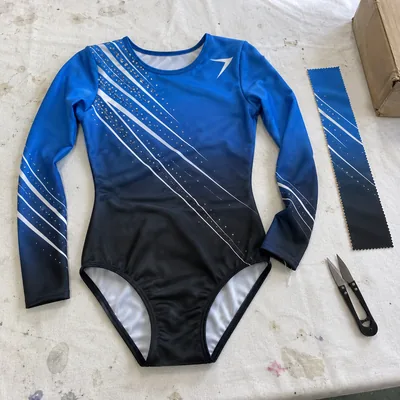 A long sleeve gymnastics leotard printed in a blue to black fade with white lines and clear stones, beside a strip of the same fabric