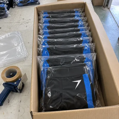 Dance team uniforms folded in clear bags and packed on edge in an open carton, beside a tape gun