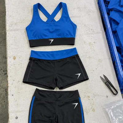 A blue crop top, black shorts with a blue waistband and black leggings laid flat, each with a white bolt