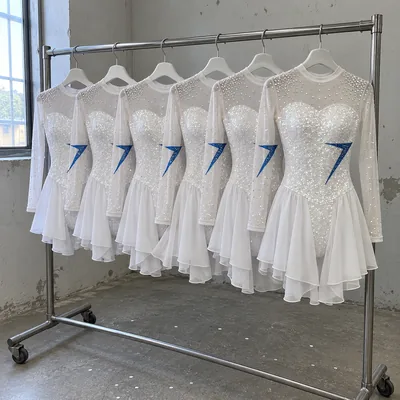Six small white competition costumes on a rail, each a little bigger than the last, with blue stone bolts