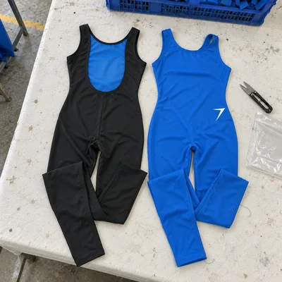 Two footless unitards laid flat: black with a blue mesh back, and blue with a white bolt at the hip