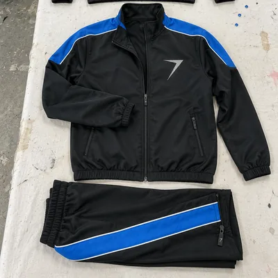 A black team jacket with blue shoulder panels and a white bolt on the chest, above black pants with a blue side stripe