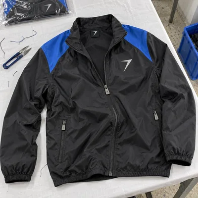 Black full-zip running jacket with blue shoulder panels and a reflective bolt on the chest