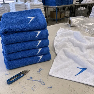 Stack of blue terry towels with an embroidered white bolt, next to a white microfiber towel with a blue bolt