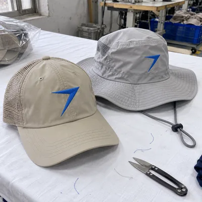 Sand fishing cap with a mesh back and a gray wide brim hat, each with an embroidered blue bolt