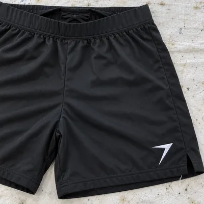 Black flag football shorts laid flat, the waistband folded down to show the drawcord inside, with a white bolt at the hem