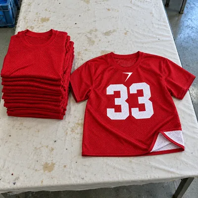 A scarlet mesh practice jersey with a white 33, laid beside a stack of folded ones