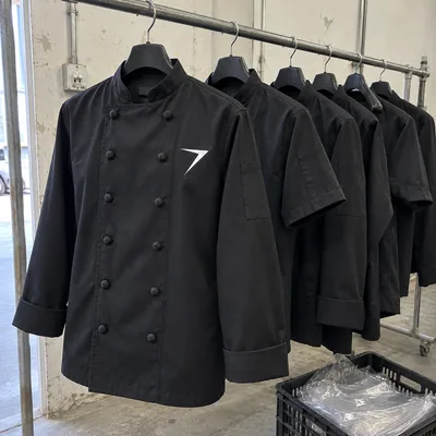 Black chef coats on a factory rail, the nearest with a white bolt on the chest and the next with short sleeves