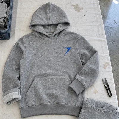 A heather gray pullover hoodie with a blue bolt on the chest, laid flat beside a folded copy