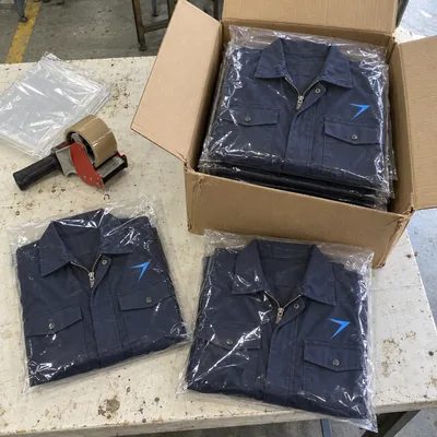 Dark navy coveralls folded in clear bags and stacked in an open carton, beside a tape gun