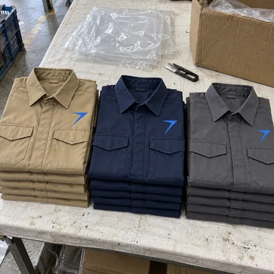 Three stacks of folded work shirts in khaki, dark navy and charcoal, each with a blue bolt above the pocket