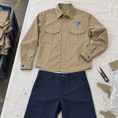 A khaki work shirt with a blue bolt above the left pocket, laid flat above dark navy work pants