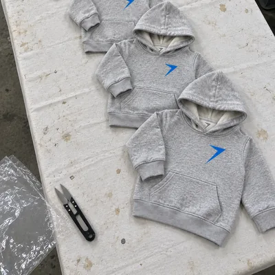 Gray kids hoodies in growing sizes laid down a factory table, with plain hood edges