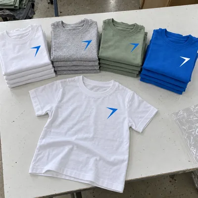 Stacks of kids tees in white, gray, sage and blue, with one white tee laid flat