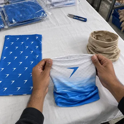Three printed neck gaiters: white fading into blue waves, blue with small white bolts, and sand
