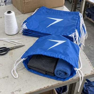 Blue drawstring bags with white cords and a white bolt, one open with a shirt and a towel inside