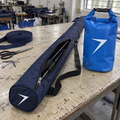 Navy padded rod bag with two rods inside and a blue roll-top dry bag, each with a white bolt