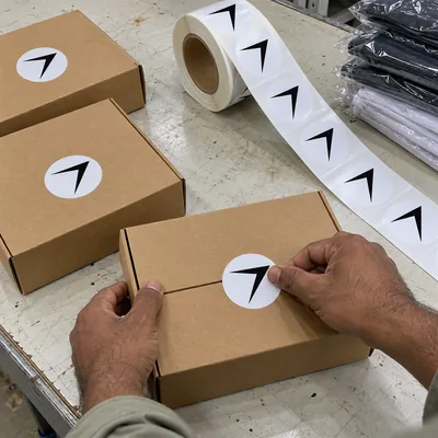 A roll of round bolt labels, and hands pressing one onto a mailer box to seal it
