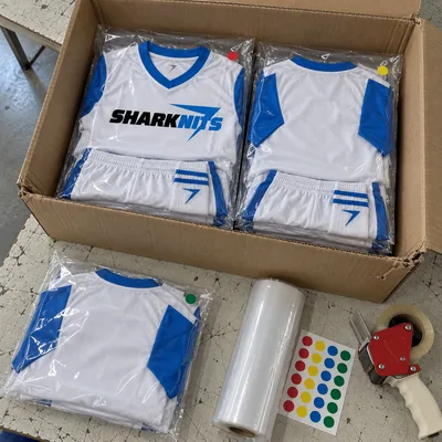 Youth soccer kits in clear bags, packed in an open carton, with color dot stickers and a roll of stretch film