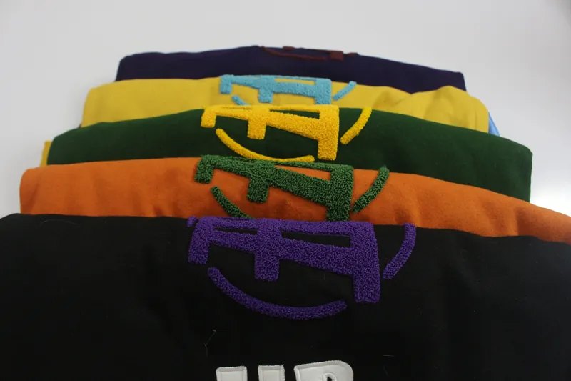 Five finished varsity jackets stacked, chenille crests showing