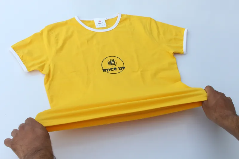Hands pull the hem of a gold Fince Up tee flat to check it